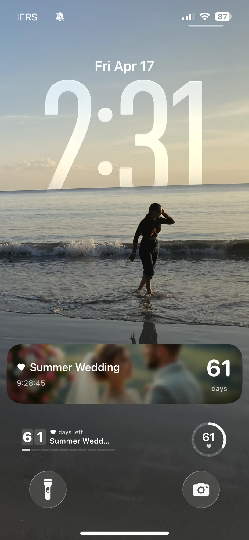 Real iPhone Lock Screen showing the same DayDrop Live Activity as a card for a wedding, 61 days away, with a photo of the couple